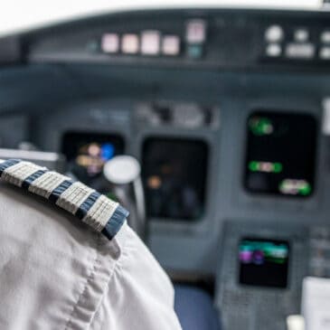 Close-up of an airline captain's shoulder with four-bar epaulets, symbolizing experience and authority, inside an aircraft cockpit with flight instruments in the background. Represents ATPL flight test preparation, advanced pilot training, and professional aviation skills development.