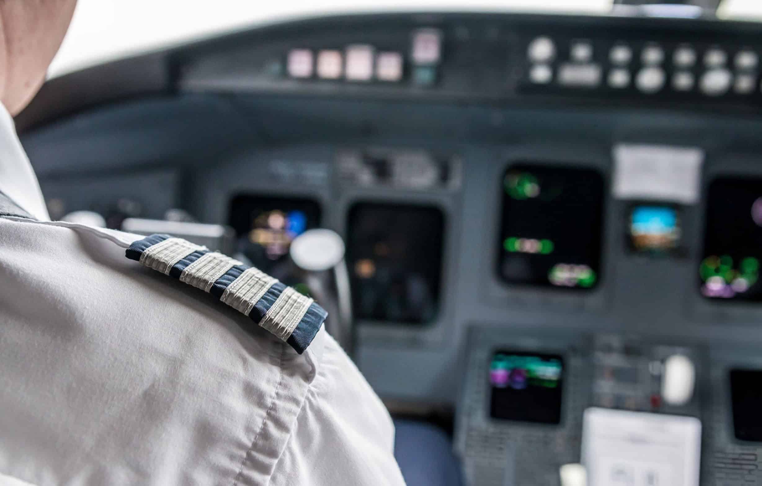 Close-up of an airline captain's shoulder with four-bar epaulets, symbolizing experience and authority, inside an aircraft cockpit with flight instruments in the background. Represents ATPL flight test preparation, advanced pilot training, and professional aviation skills development.